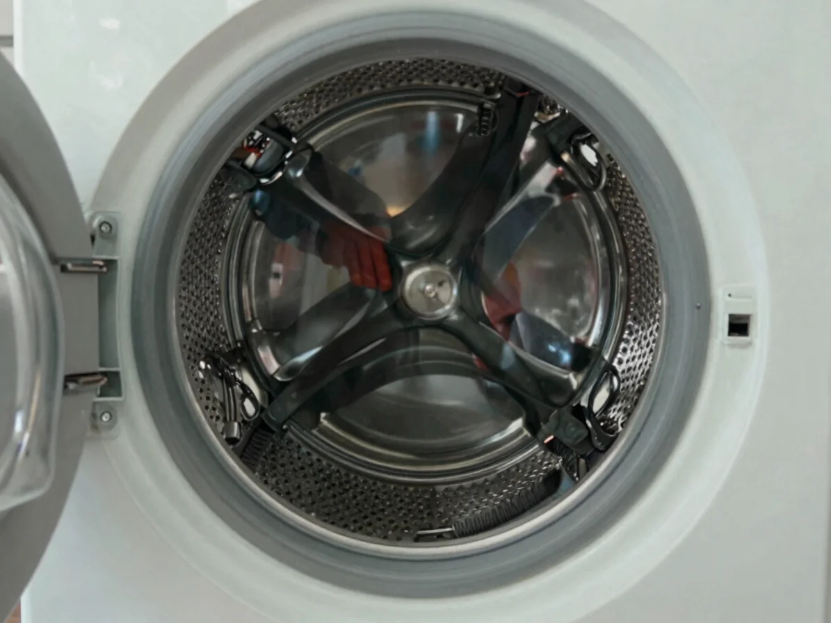 Technician examining the drum and drive belt of a front-loading washing machine, wide framing of a service room, documen